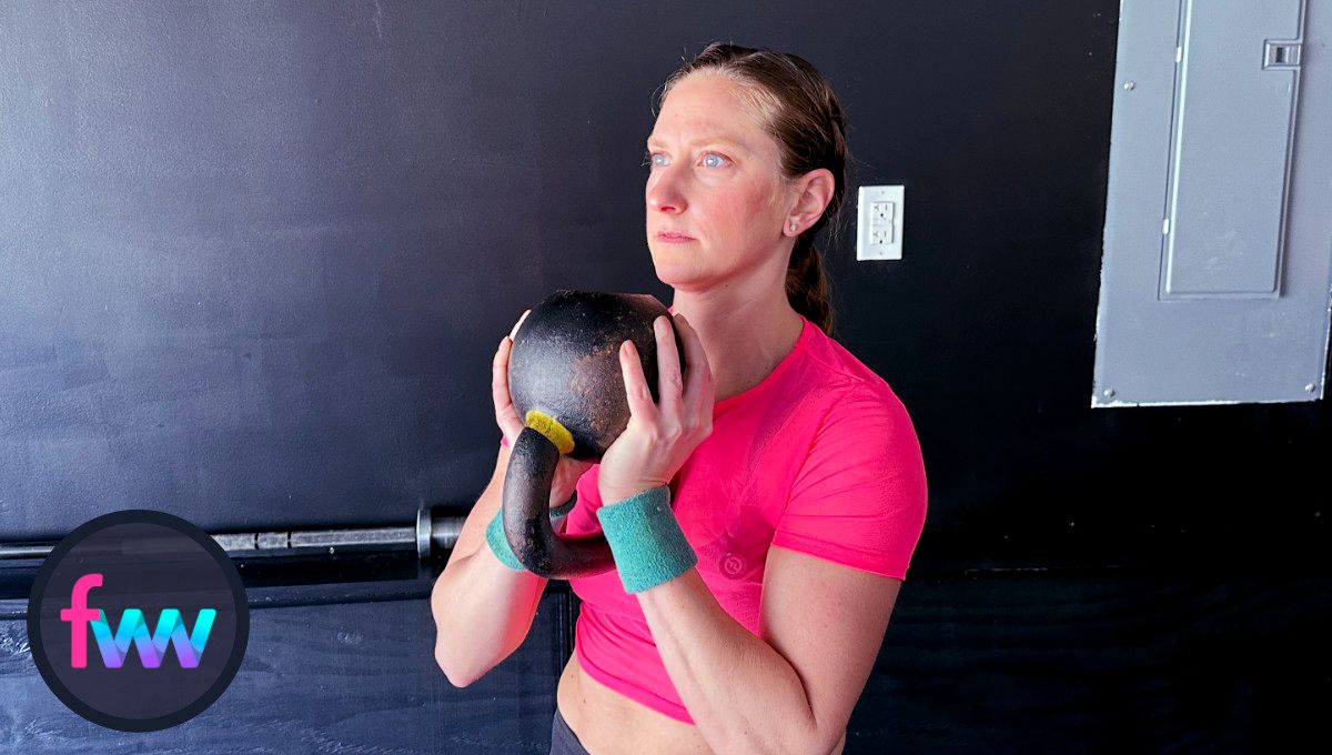 Kindal holding the kettlebell by the bell with the handle between her arms. She is in balance with a tight core ready to press it up over her head.