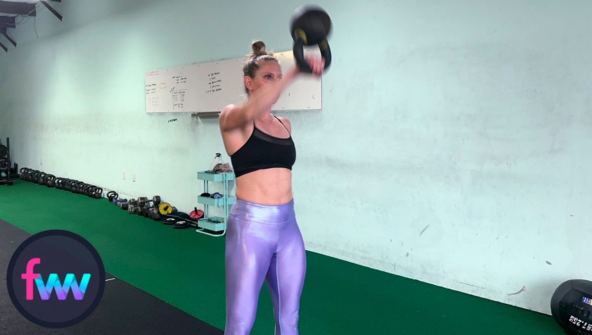 Kindal showing the kettlebell snatch punch where she punches around the kettlebell so it lands softly and correctly on her arm.