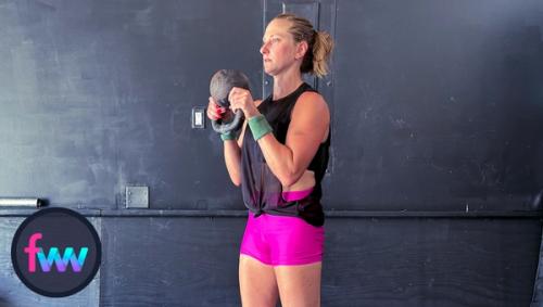 Kindal at the top of the kettlebell curl. She is gripping the kettlebell hard and pulling all the way to her chest.