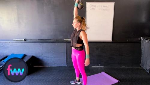 Kindal at the top of the kettlebell snatch and pressing the kettlebell high through her shoulder.