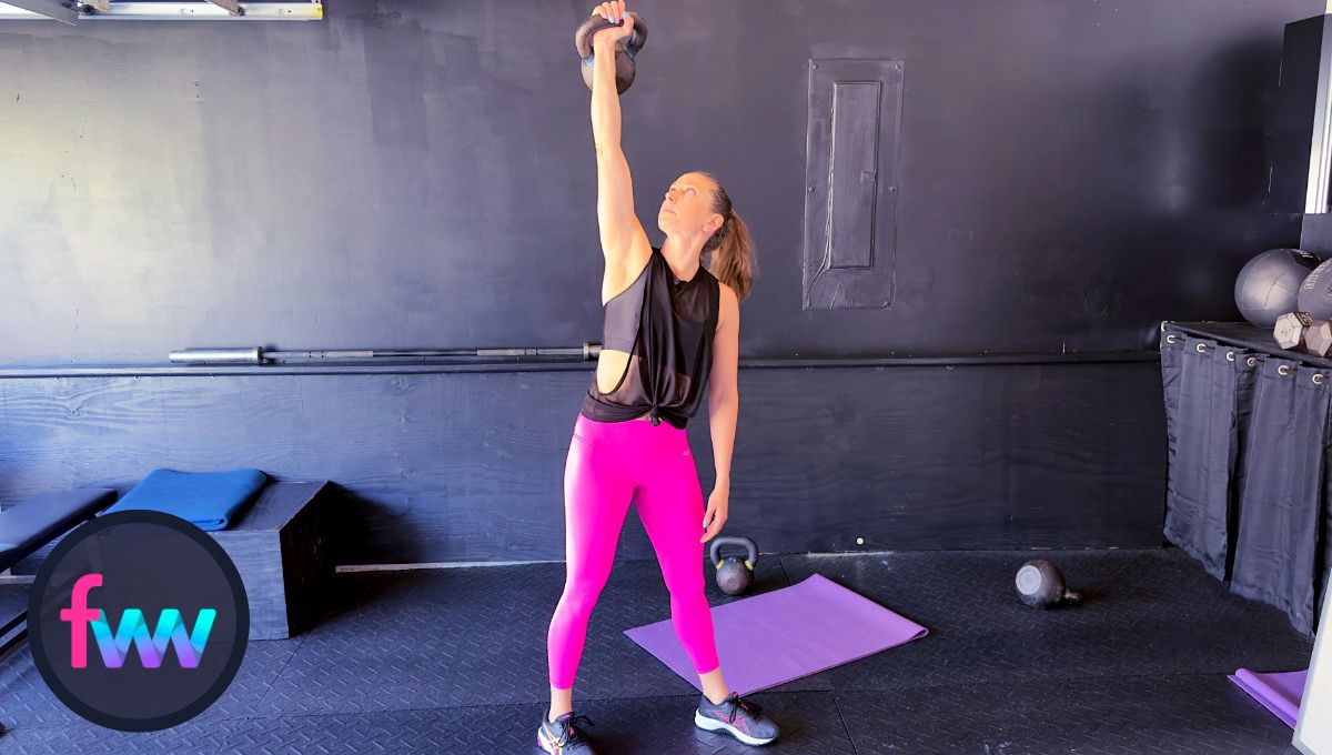 Kindal presses the kettlebell over head and looks at the bell as she gets ready to hip hinge off to the side while bracing her core tight.