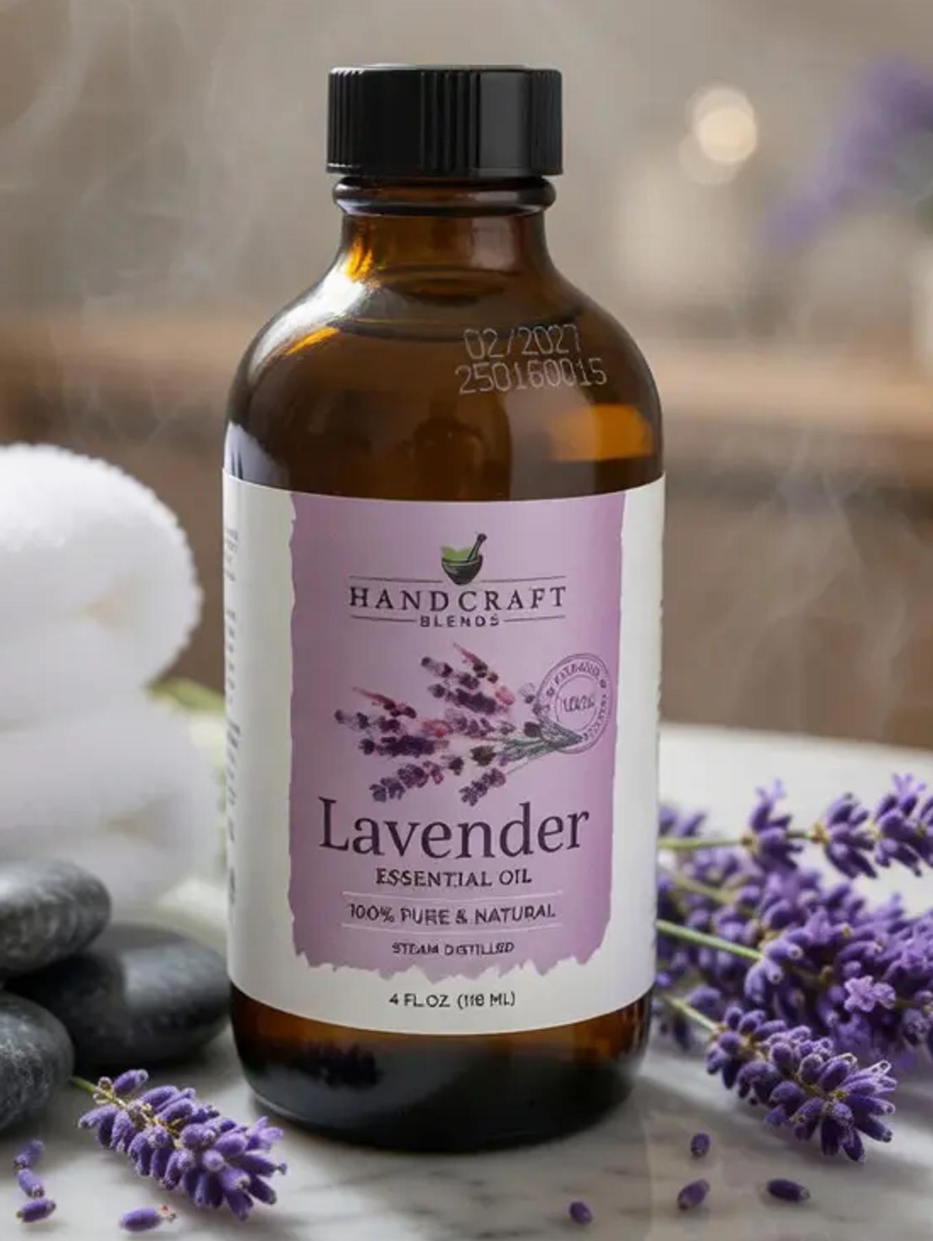 Lavender essential oil bottle with steam rising, placed on a marble surface beside folded towels, smooth black stones, and fresh lavender sprigs in a spa-like setting.