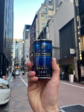 A can of Dydo Blend Demitasse held up against the background of a narrow street in Tokyo