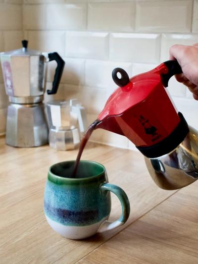 The Bialetti Moka Induction pouring coffee into a blue and green mug.