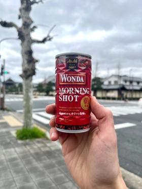 A can of Wona Morning Shot held up against the background of a Kyoto street