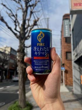 A can of Kirin Fire Kiriman held up against the background of a street.