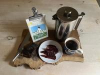 A french press, a pack of moomin troll coffee, a moomin troll mug, and a plate of sliced cured reindeer meat.