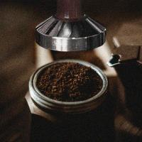 A heap of coffee grounds in a moka pot basket about to be tamped by a tamper.