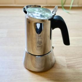 A shiny steel Bialetti Venus moka pot on a wooden kitchen surface