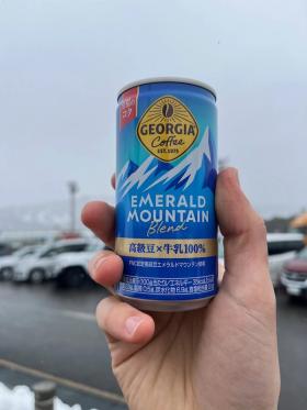 A can of Georgia Emerald Mountain Blend fittingly held up against the backdrop of a snow storm in a parking lot.