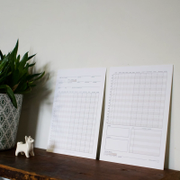 Two tasting cards on a shelf leaning against a white wall, with a small white porcelain dog looking at the cards.