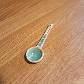 A small ceramic spoon with patches of green glaze.