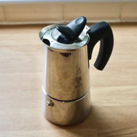 A shiny metallic moka pot with a curved black handle.