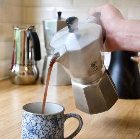 A 6 cup Bialetti Moka Express pouring coffee into an ornate blue and grey mug.