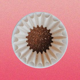 A pour over cone with a paper filter full of ground coffee, viewed from above, on a pink gradient background,