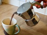 Dark coffee being poured from the Alessi Moka 3 Cup into a multi-coloured coffee cup.