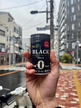 A can of Ito En W Coffee Black held up agains the backdrop of a Tokyo street.