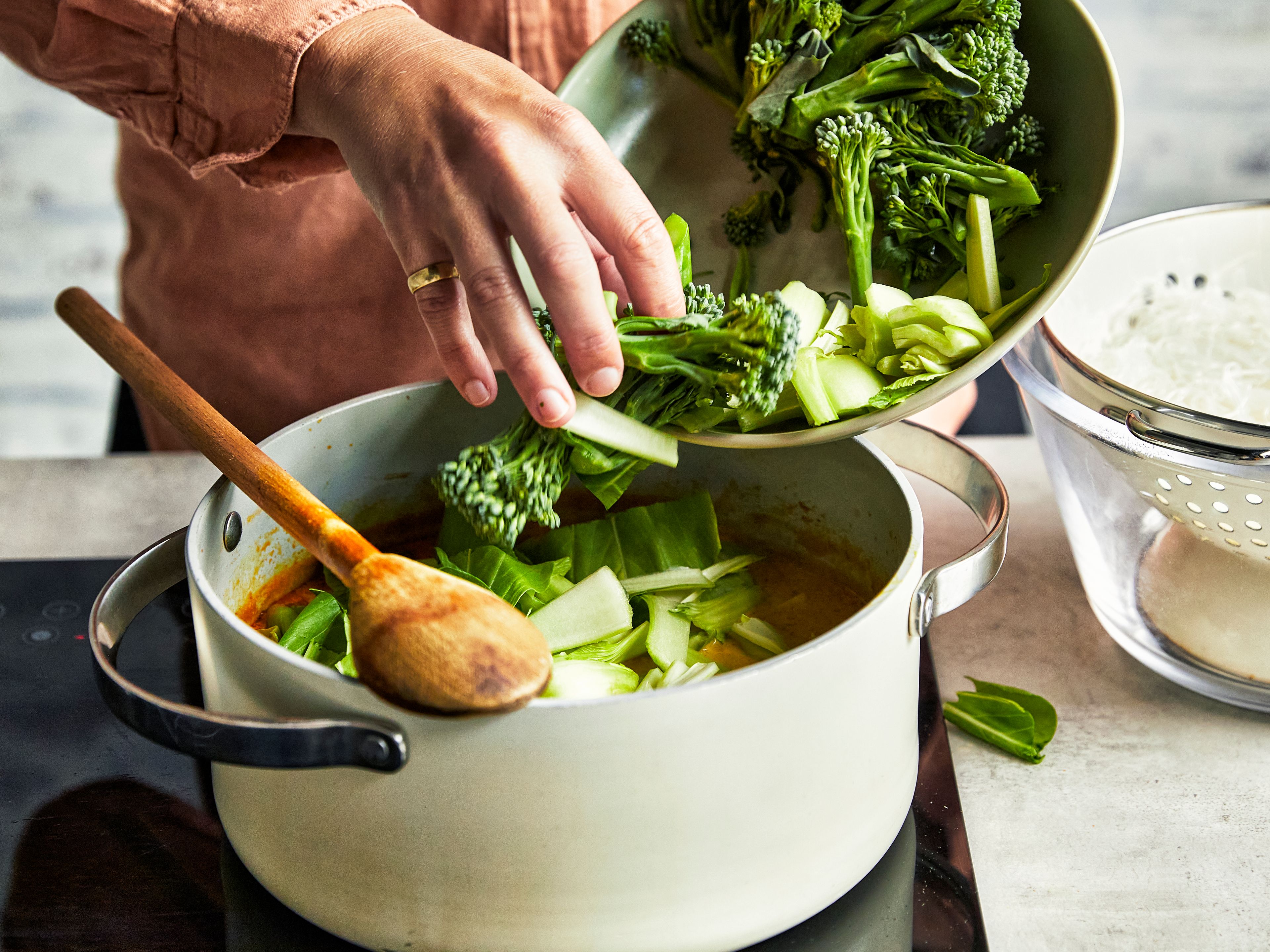 Woman cooking laksa in a pot and adding broccoli florets