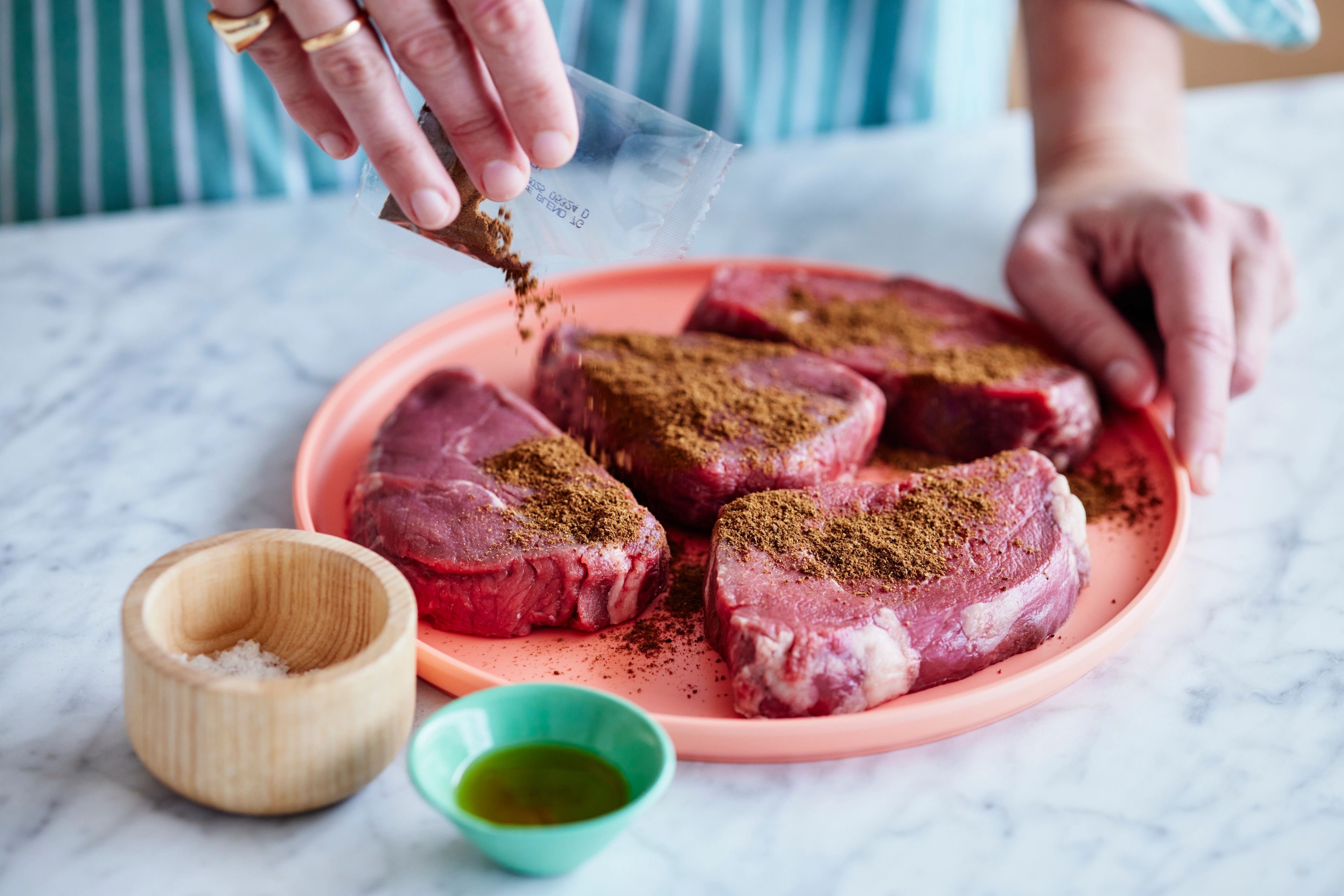 fresh quitelike beef steak being seasoned on kitchen counter