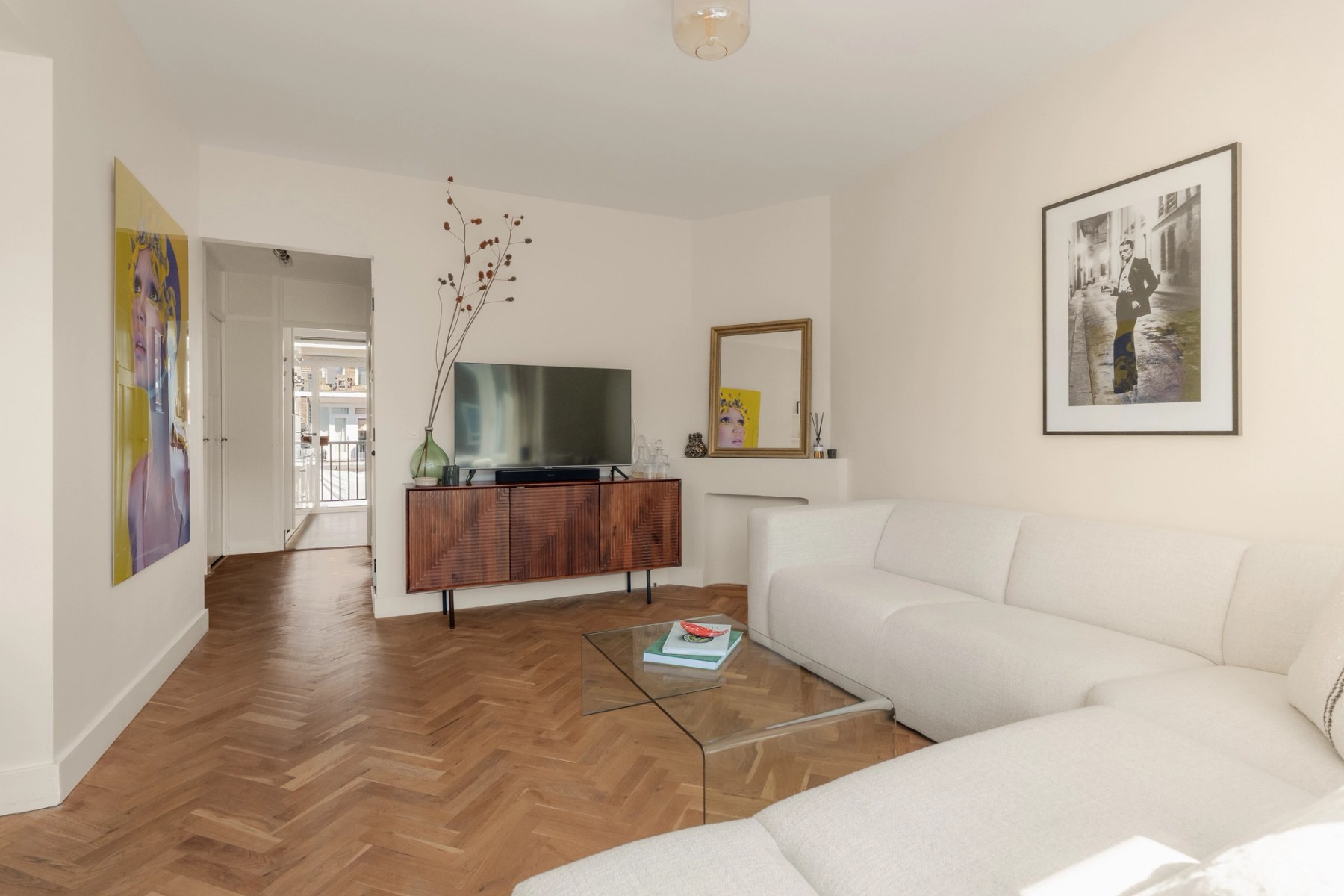 Woonkamer met witte bank, glazen salontafel en kunst aan de wand