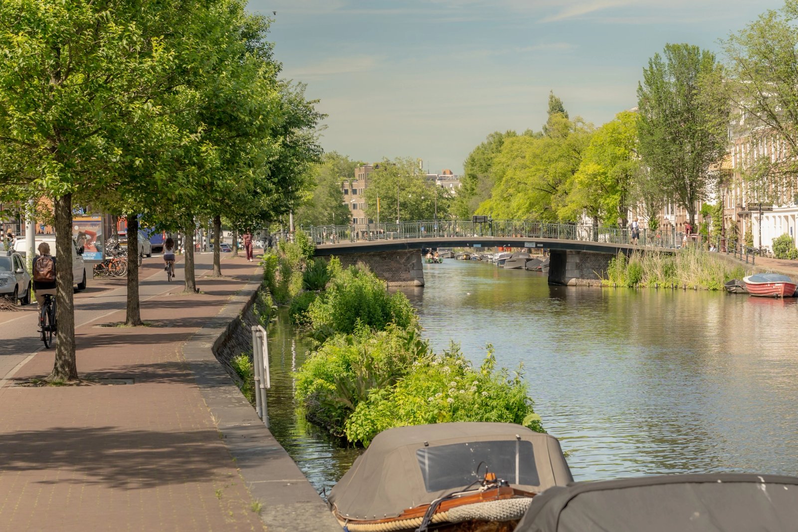 Amsterdamse gracht met bomen langs de kade, een brug en aangemeerde bootjes