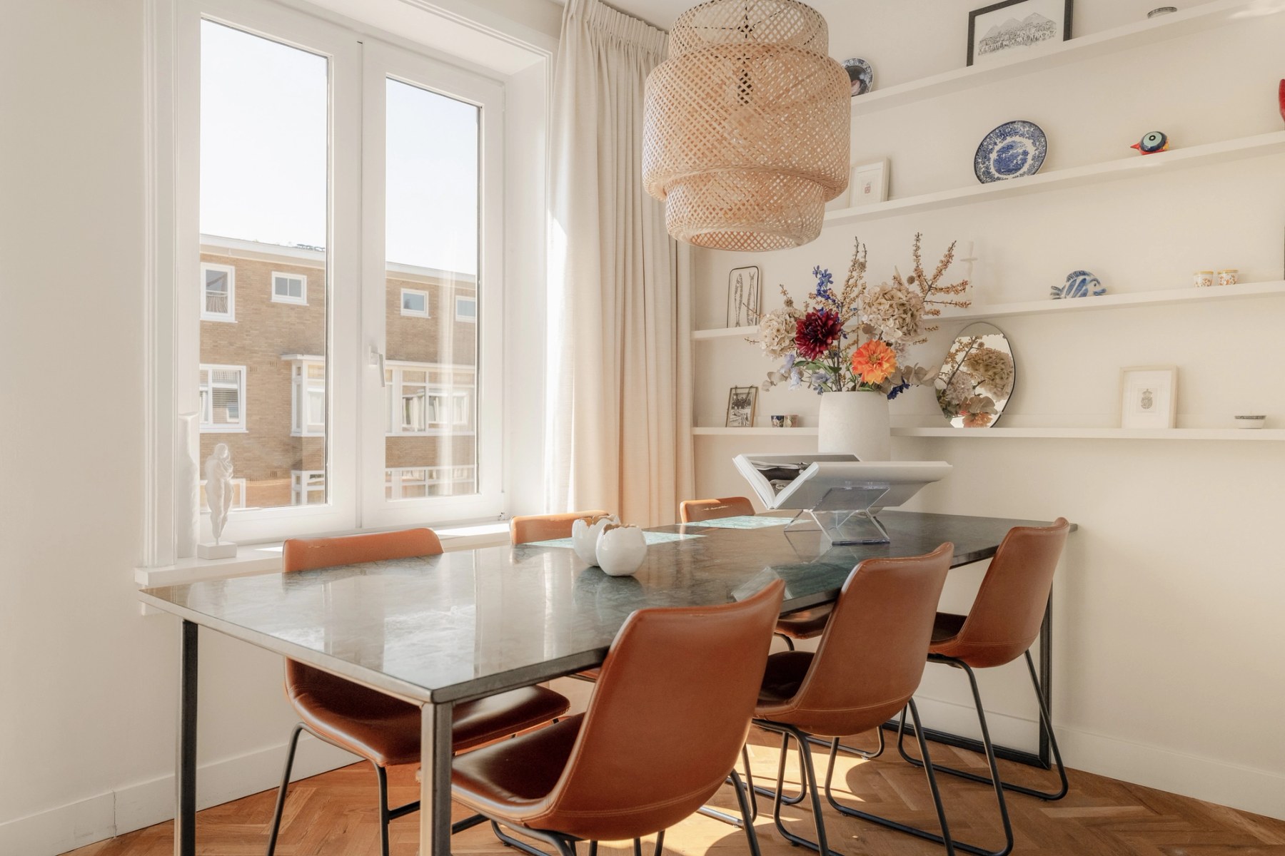Eethoek met leren stoelen, rieten hanglamp en wandplanken naast het raam