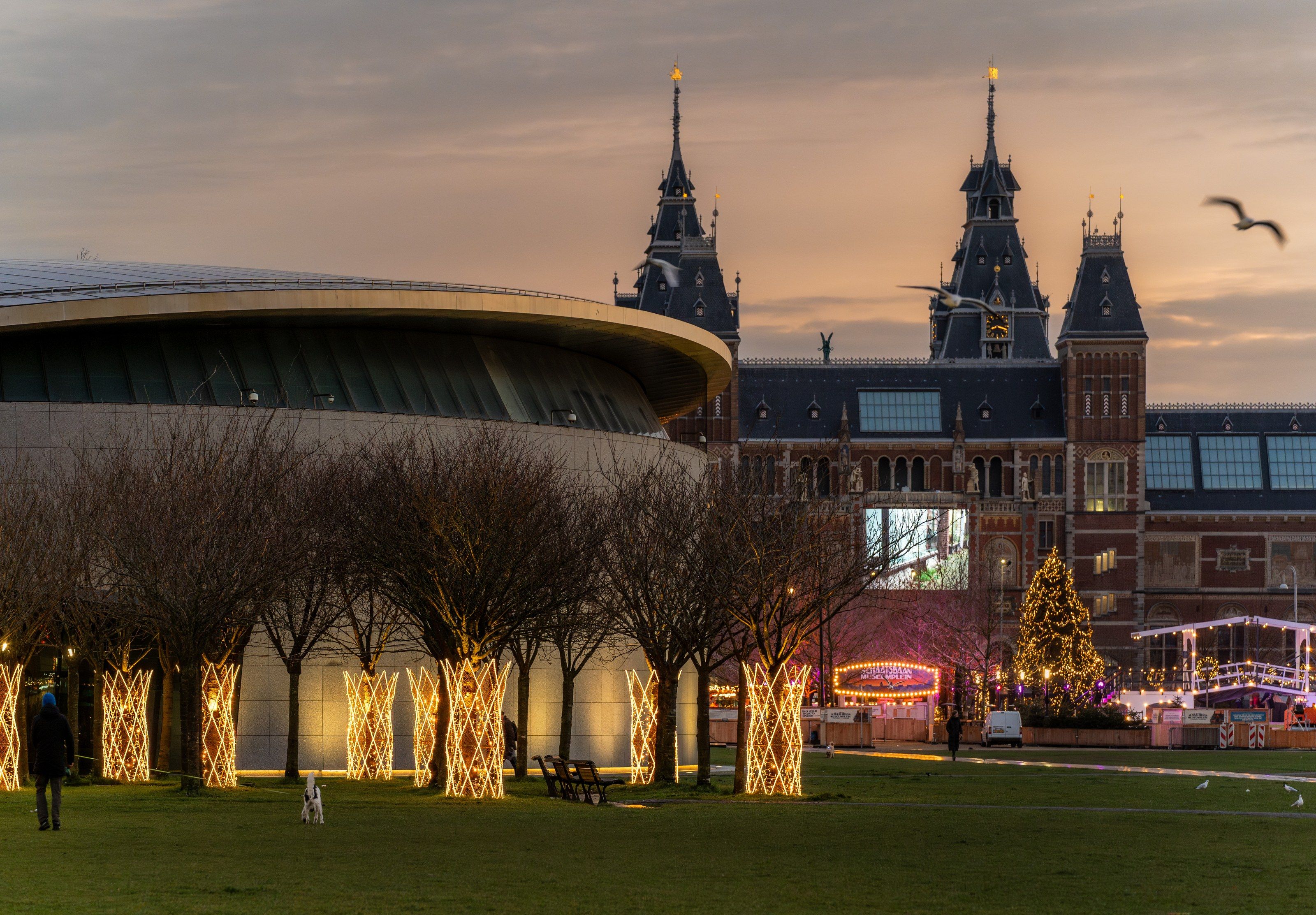 Met licht omwikkelde bomen naast het Van Gogh Museum, met het Rijksmuseum erachter