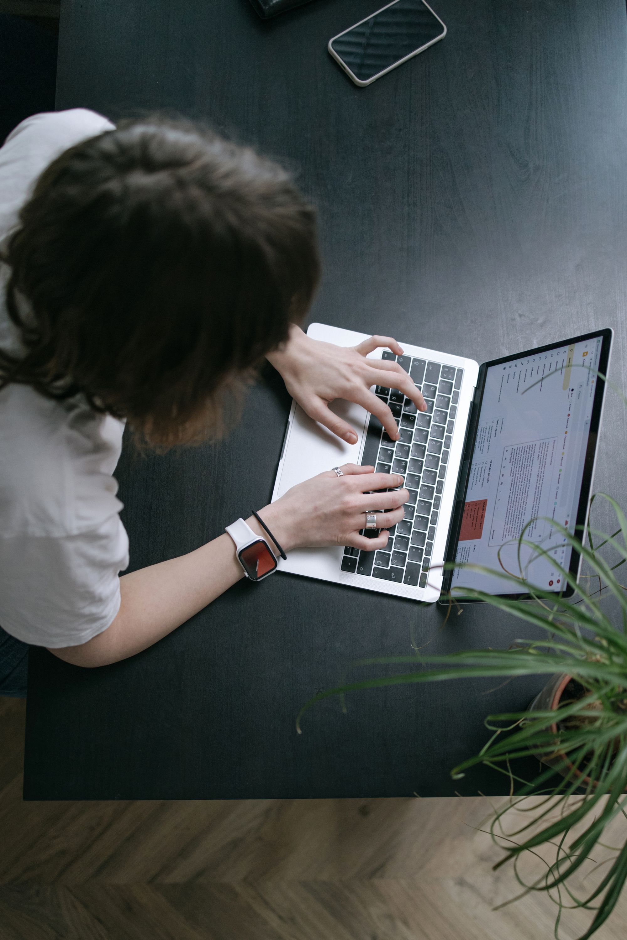 A person working on a laptop beside a phone at a wooden desk