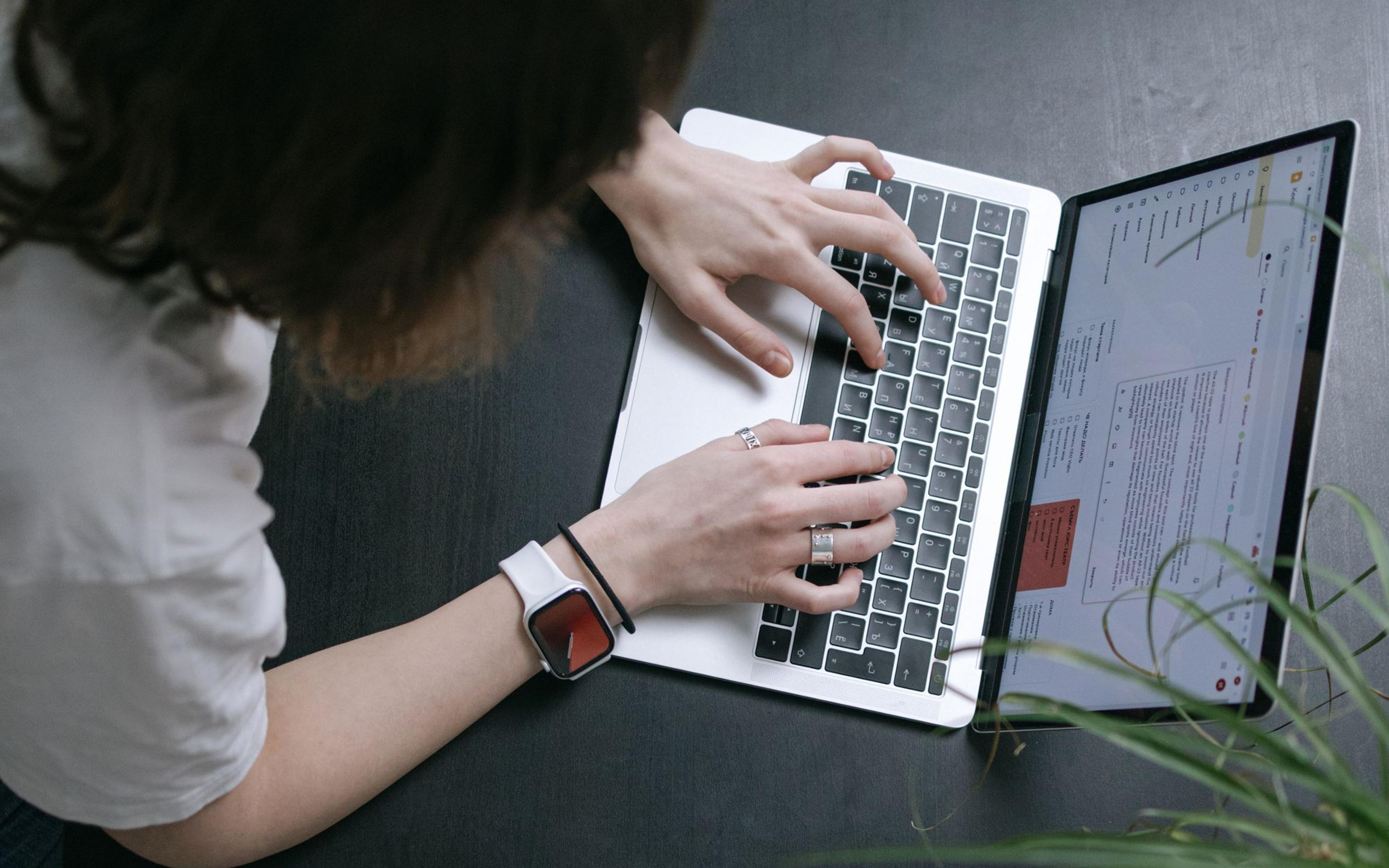 A person working on a laptop beside a phone at a wooden desk