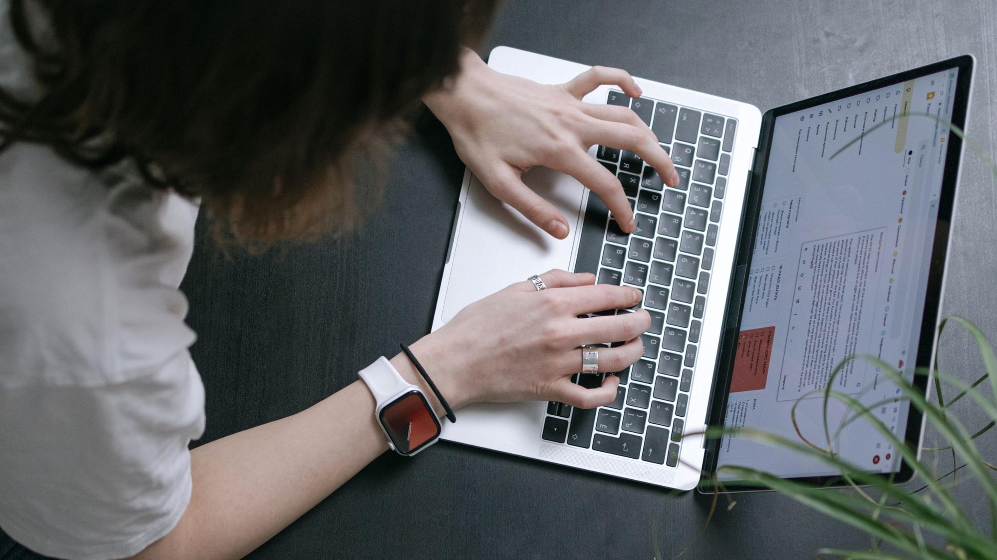 A person working on a laptop beside a phone at a wooden desk