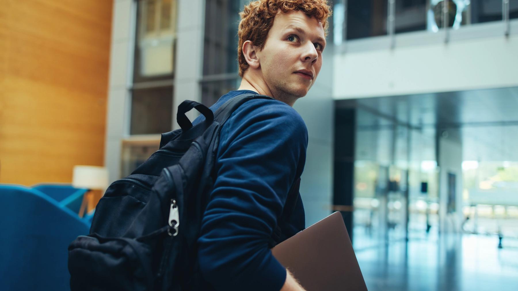 En ung voksen som holder laptop i hånden og ser nyskjerrig ut
