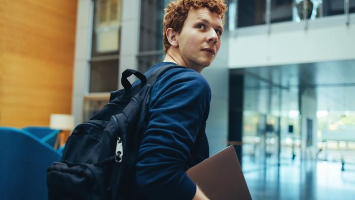 En ung voksen som holder laptop i hånden og ser nyskjerrig ut