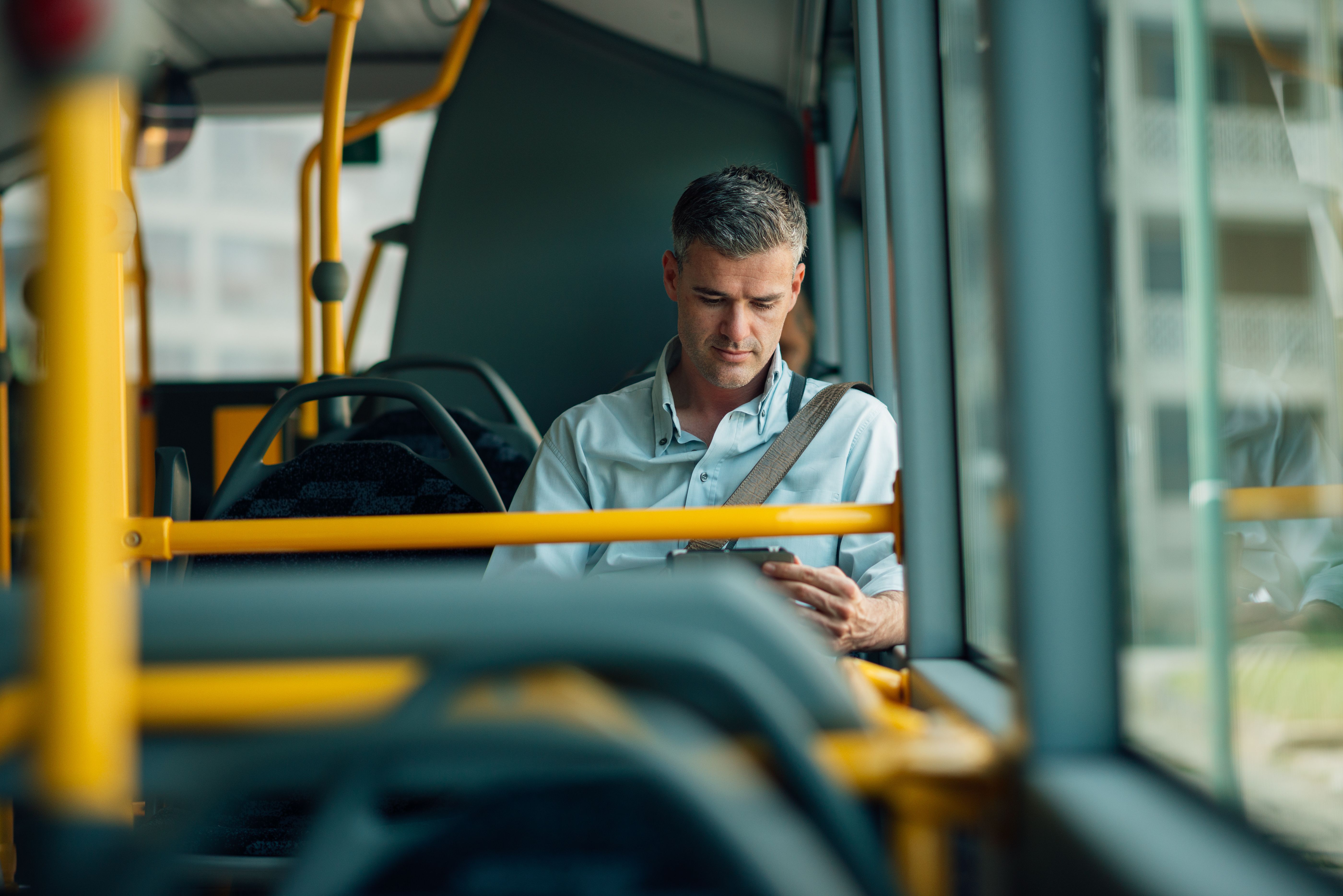 Mann sitter å ser på nettbrettet sitt i bussen