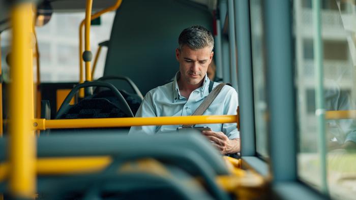 Mann sitter å ser på nettbrettet sitt i bussen