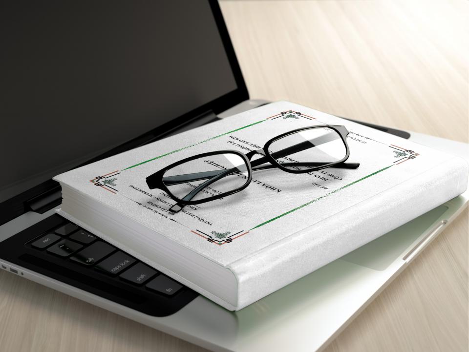 Lesebrille liegt auf einem aufgeschlagenen Buch neben einem Laptop