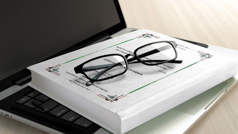 Lesebrille liegt auf einem aufgeschlagenen Buch neben einem Laptop