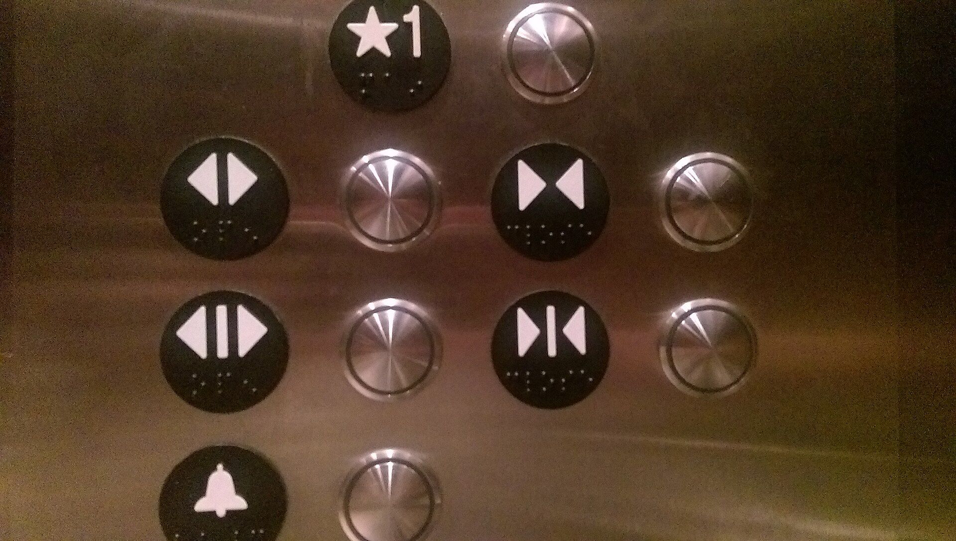 Bedienfeld in einem Aufzug mit runden Tasten, die nur Pfeilsymbole und Braille-Punkte tragen, aber keine Beschriftung