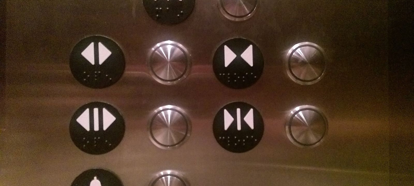 Bedienfeld in einem Aufzug mit runden Tasten, die nur Pfeilsymbole und Braille-Punkte tragen, aber keine Beschriftung