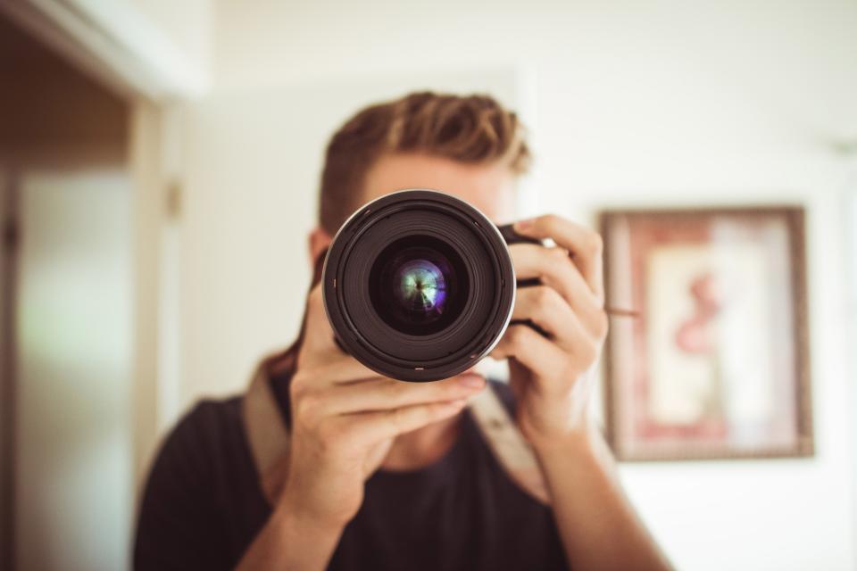 Mann fotografiert mit einer Spiegelreflexkamera direkt in die Kamera