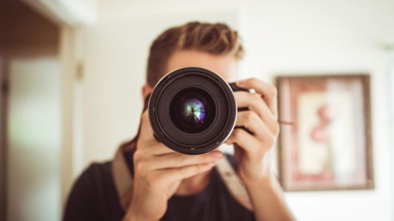Mann fotografiert mit einer Spiegelreflexkamera direkt in die Kamera