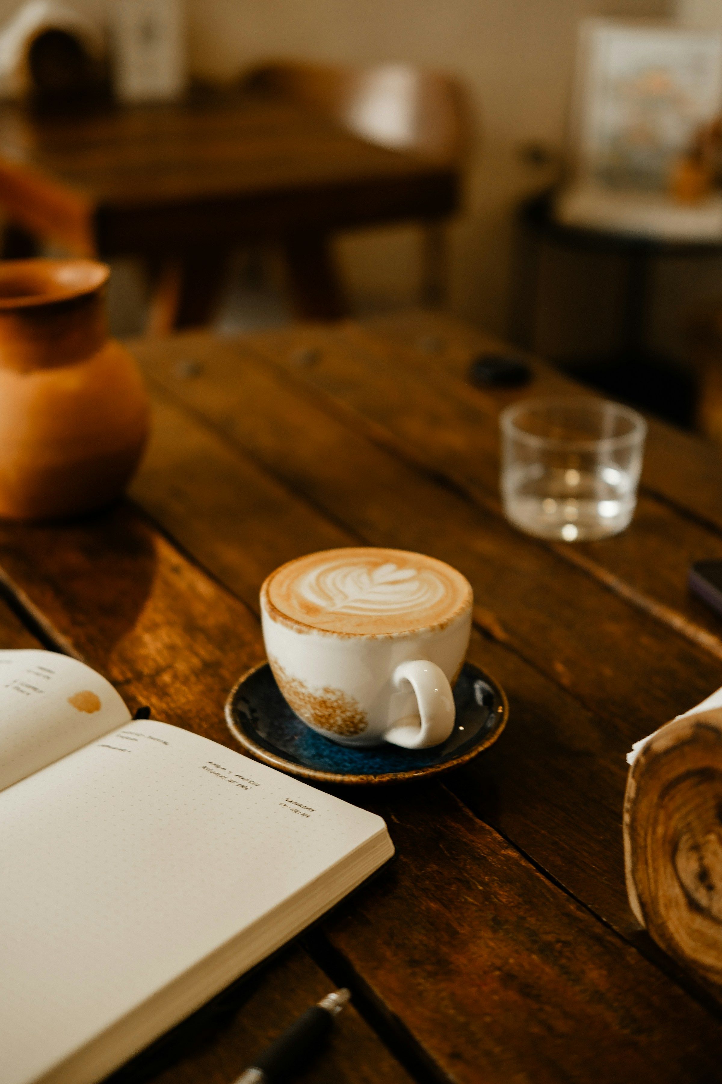 Cappuccino und aufgeschlagenes Notizbuch auf einem Holztisch im Café