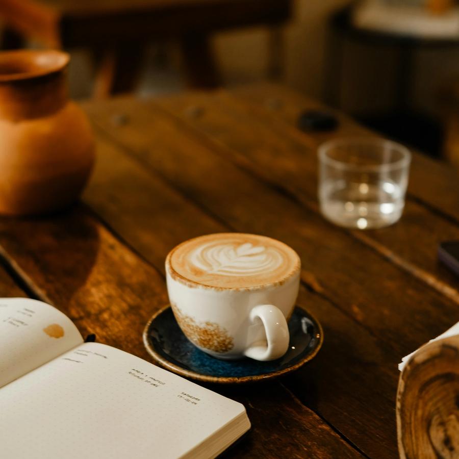 Cappuccino und aufgeschlagenes Notizbuch auf einem Holztisch im Café