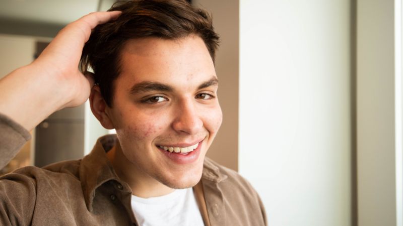 Junger Mann lacht und fährt sich durch die Haare