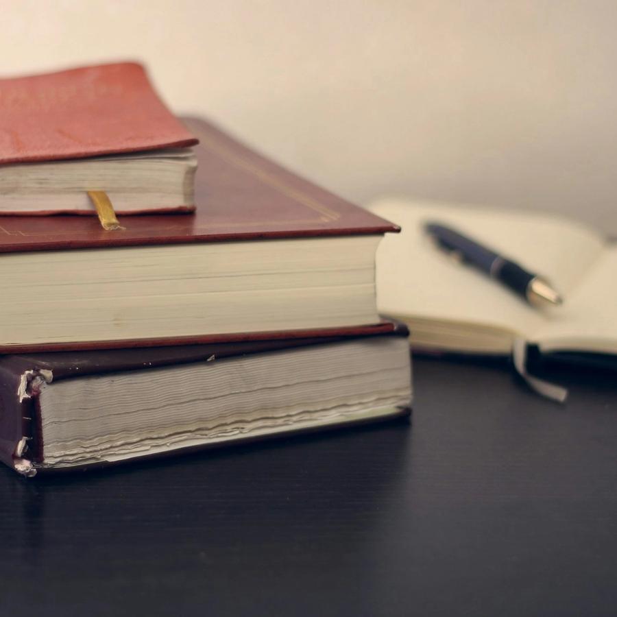 Gestapelte Bücher neben einem aufgeschlagenen Notizbuch mit Füller