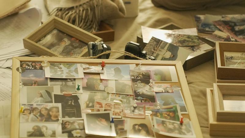 Pinnwand aus Kork voller Fotos, daneben Bilderrahmen und weitere lose Abzüge auf einem Tisch