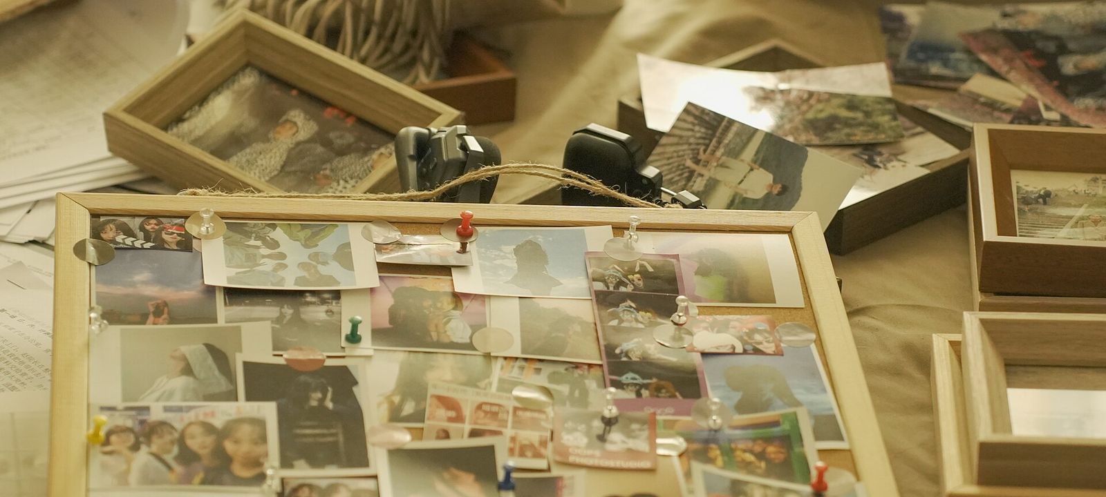Pinnwand aus Kork voller Fotos, daneben Bilderrahmen und weitere lose Abzüge auf einem Tisch