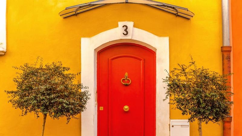 Rote Haustür in einer gelben Hauswand mit zwei Bäumchen