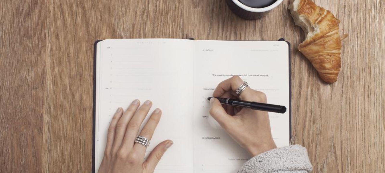 Hände schreiben mit Stift in ein Notizbuch auf einem Holztisch