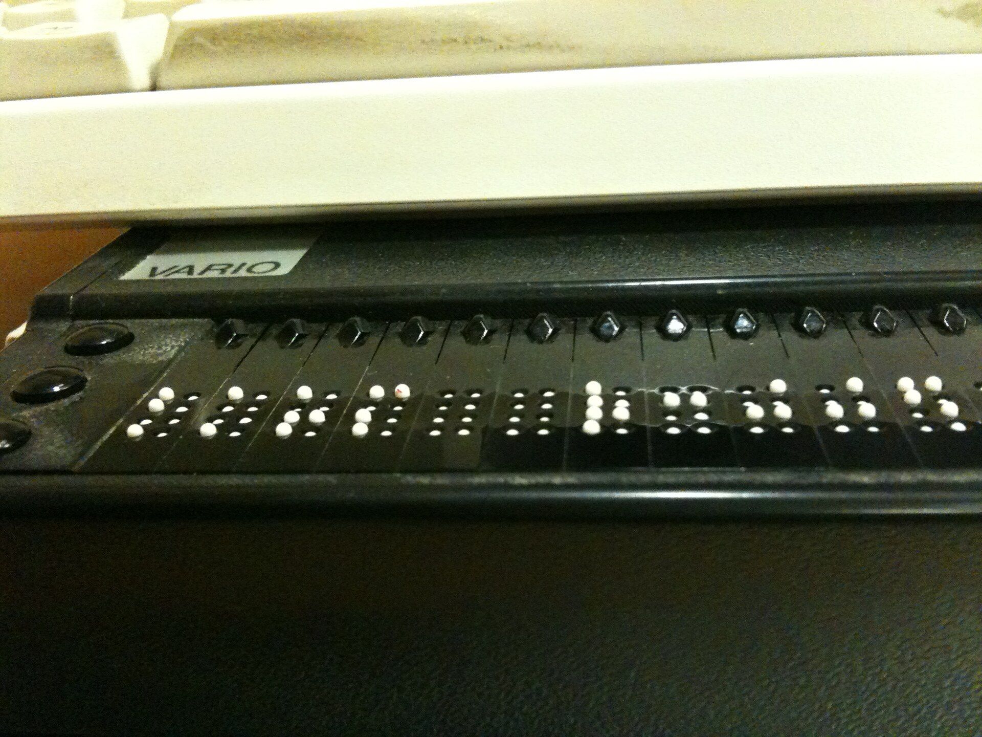Nahaufnahme einer Braillezeile unter einer Computertastatur, die erhabenen weißen Punkte bilden Buchstaben in Blindenschrift