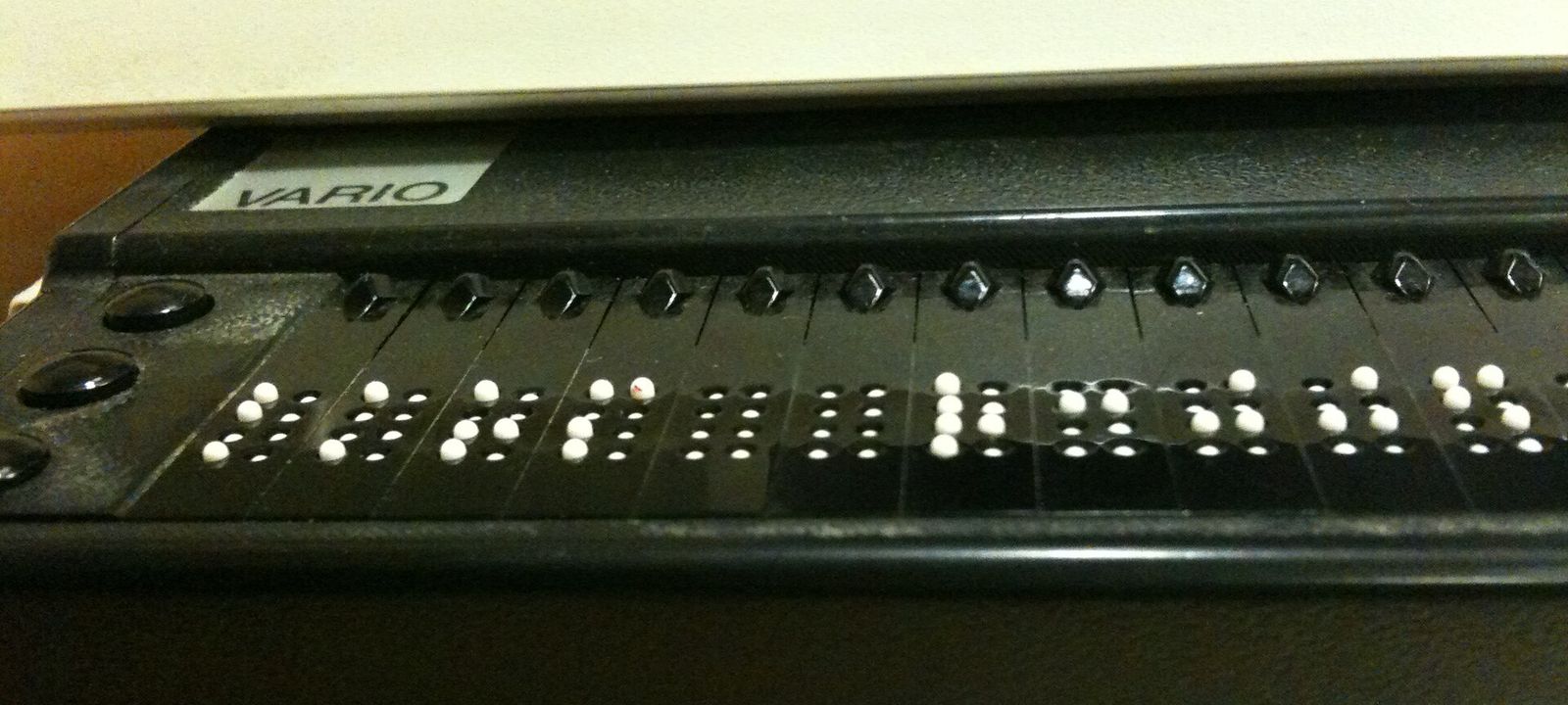 Nahaufnahme einer Braillezeile unter einer Computertastatur, die erhabenen weißen Punkte bilden Buchstaben in Blindenschrift